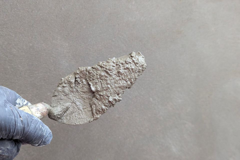 Main gantée tenant une truelle chargée d'enduit devant un mur lisse